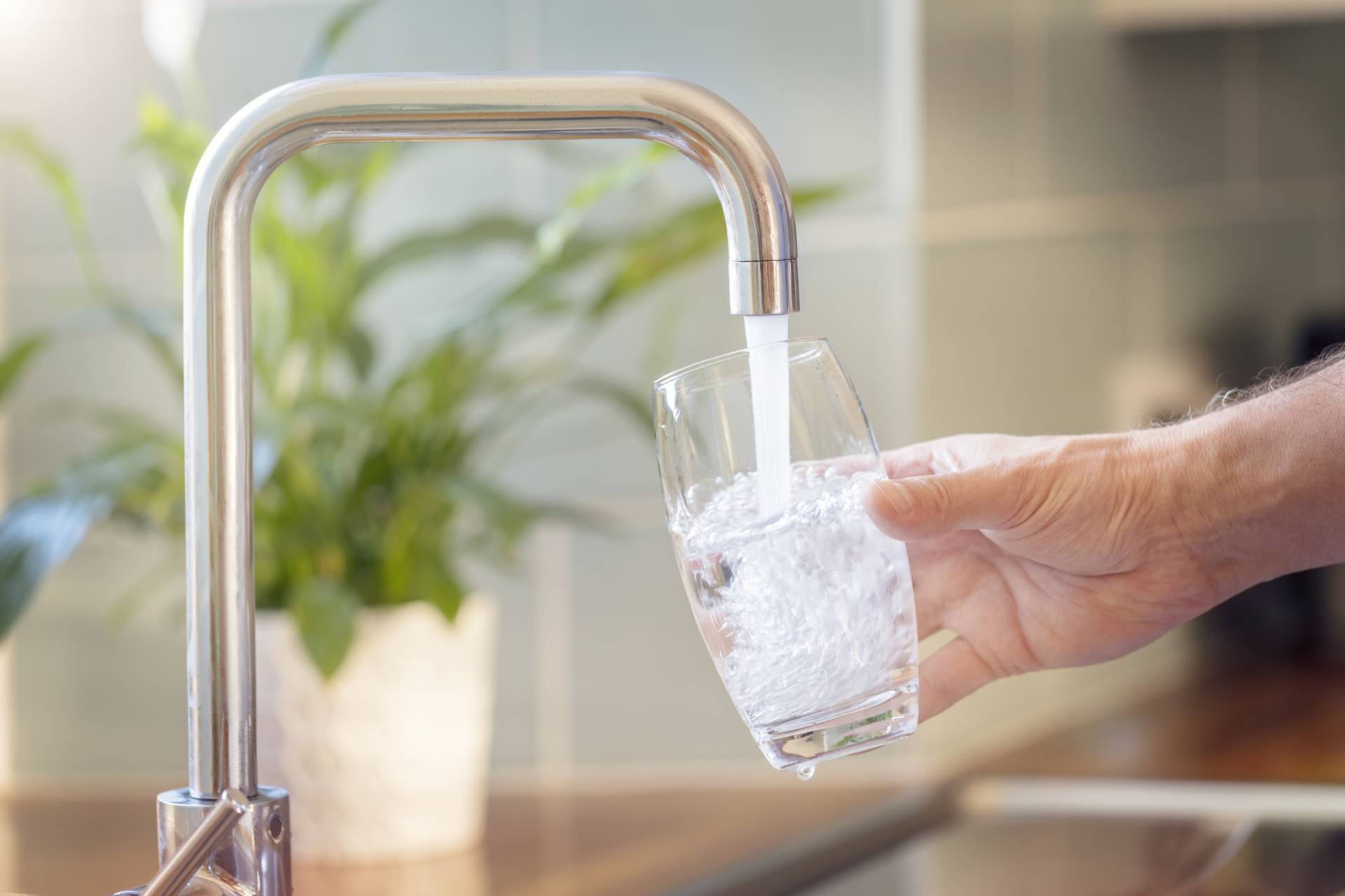 A person filling a glass from a kitchen tap with softened water.