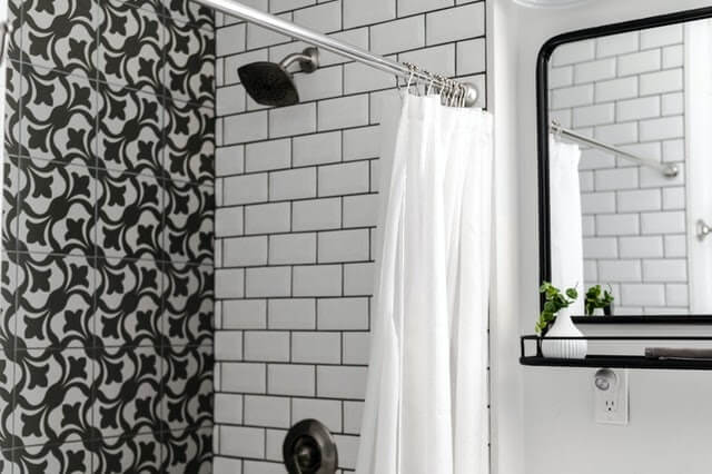 tiled bathroom with a shower head and curtain showing effects of hard water