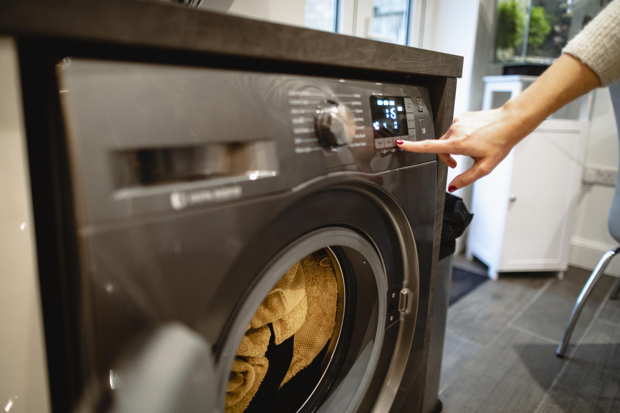 A close-up shot of an unrecognisable caucasian woman pressing a button on her washing machine.